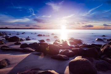 sunset rocks beach seascape, long exposure, bright sunflare reflection, high contrast, blue sky,...