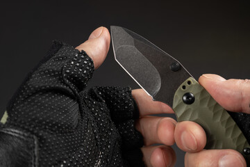 Hand in tactical glove, holding folding knife, close up