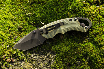 Tactical folding knife for survival on moss background