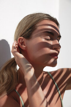 Young Woman with Shadow of Palm Leaves on White Wall