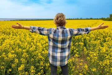 Woman in rapeseed field blooming in the summer. Back view of a blonde girl enjoying sun in blossom...