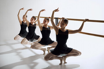 Elegance in training. Beautiful, focused teen girls, ballet dancers standing at barre and practicing against grey studio background. Concept of ballet, art, dance studio, classical style, youth