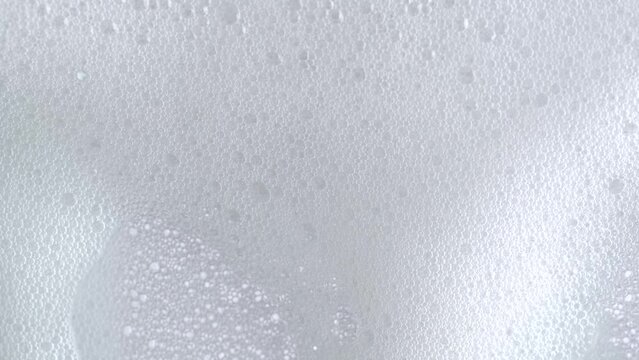 Macro shot of white soap suds flowing down of glass. Shower concept. Soap bubbles on window glass. Cleaning windows, hygiene, cleanup, washing.