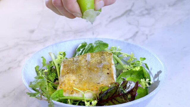 Close-up of man's hand squeezing lime juice on white fish, pike-perch zander and salad. 4k Slow motion 100fps video.