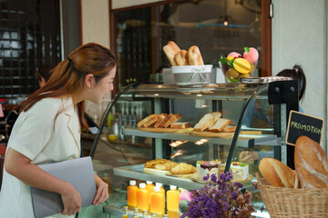 Asian female customer holding a laptop. Choosing bakery and bread, coffee. The cafe is a small...
