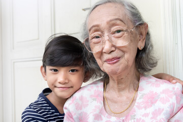 Cute Asian boy embracing his grandmother while smiling and posing to camera