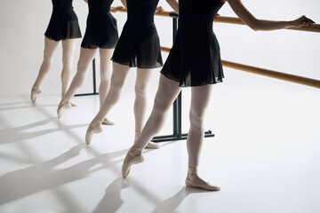 Elegance on pointe. Cropped image of female ballet dancer standing in a row at barre, practicing against grey studio background. Concept of ballet, art, dance studio, classical style, youth © master1305
