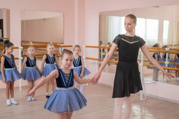 Naklejka premium Children's ballet school. Caucasian woman teaching ballet to little girls. 
