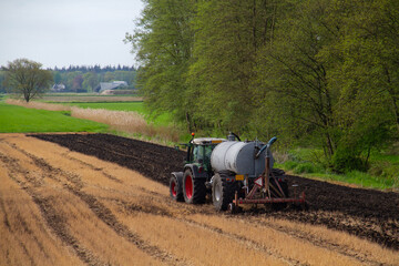 Tractor with slurry tank preparing field treated with glyphosate for cultivation by applying manure...