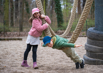Cute children having fun outdoors. They ride on a swing. A girl stands near a rope swing. The boy...