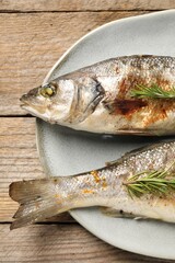 Delicious baked fish and rosemary on wooden table, top view