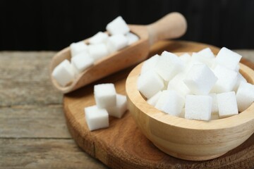 White sugar cubes in bowl and scoop on wooden table, closeup