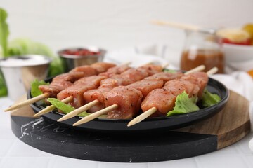 Wooden skewers with cut raw marinated meat on white tiled table, closeup