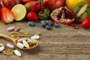 Different vitamin pills and fresh fruits on wooden table. Space for text