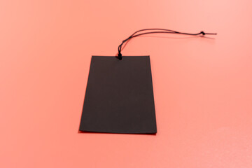 Black label with black cord with space for writing on a pink background. Black label on a pink...