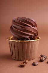 Delicious chocolate cupcake and coffee beans on brown background, closeup