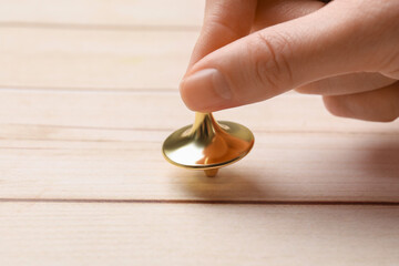 Woman playing with metal spinning top at light wooden table, closeup