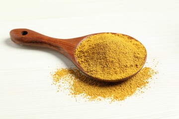 Curry powder in spoon on white wooden table