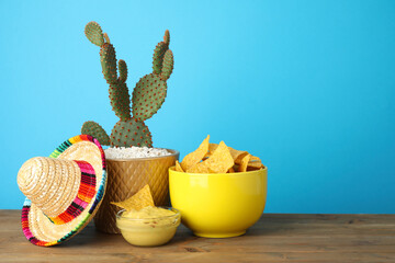 Mexican sombrero hat, cactus, nachos chips and guacamole in bowls on wooden table against light...