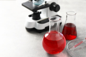 Laboratory analysis. Flasks with red liquid, petri dish and microscope on light grey table