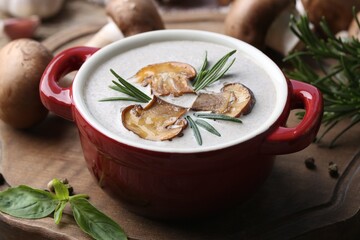 Delicious homemade mushroom soup in ceramic pot and fresh ingredients on wooden table