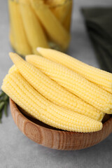 Tasty fresh yellow baby corns in bowl on grey table, closeup
