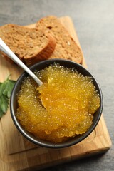 Fresh pike caviar in bowl and bread on grey table, closeup