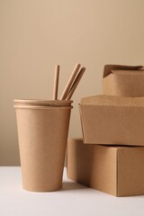 Eco friendly food packaging. Paper containers and straws on white table against beige background
