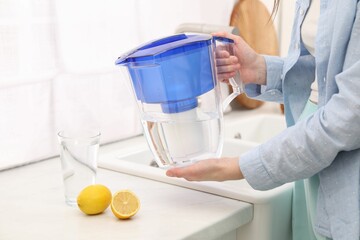 Woman with water filter jug in kitchen, closeup