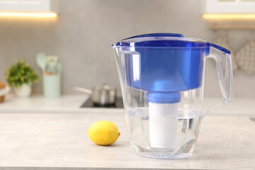Water filter jug and lemon on light grey table in kitchen, space for text