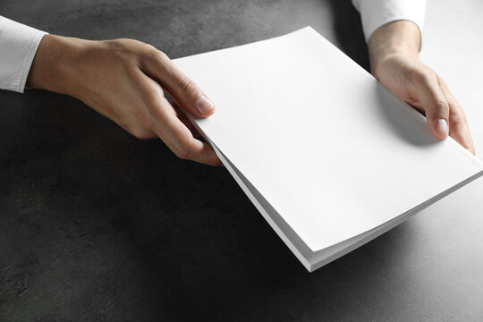 Man holding blank notebook at black textured table, closeup. Mockup for design