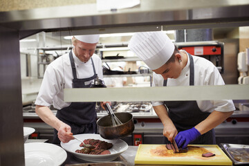 Chefs, sausage and men cutting in kitchen of restaurant for dinner, lunch or supper with...