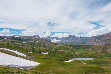 Scenic awesome landscape with big snowfield and alpine lake among green hills and rocks with view...