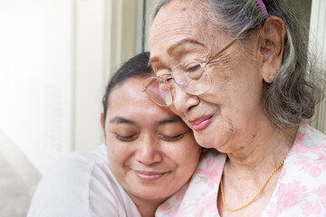 A happy Asian mature adult daughter hugging her old mother when visiting her at home
