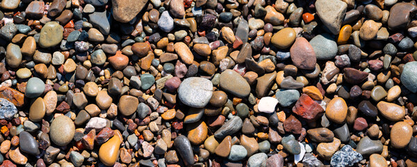 Colorful wet pebble panorama on Carpinteria Beach in California (USA). Stones in the surf area of the Pacific Ocean that have been ground round by erosion into beige, gray, brown, reddish and bluish.