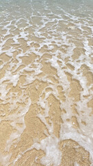 a close up of a wave crashing onto a sandy beach.
