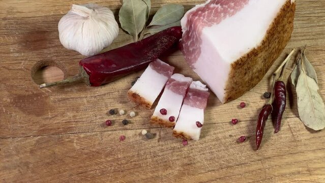 Partly sliced salted pork fatback among spices on cutting board