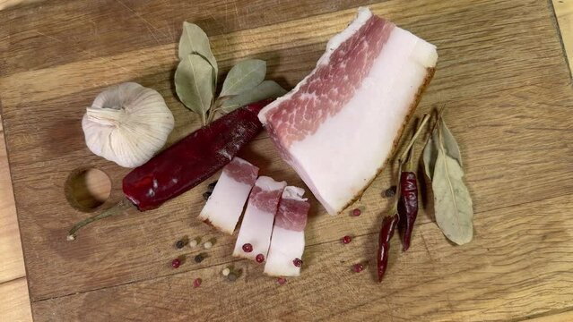 Partly sliced salted pork fatback among spices on cutting board