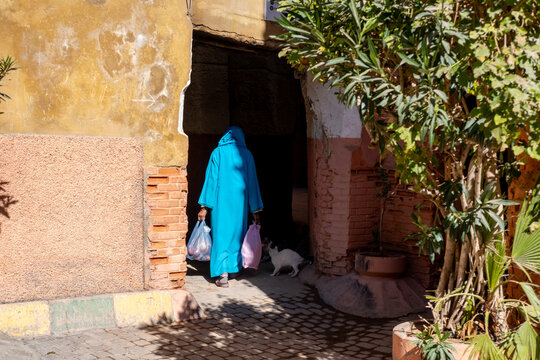 muslim woman with bags in hands in traditional long attire walks down street Red City Marrakech, authentic urban African landscape, daily activities people