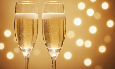 Two glasses of white sparkling wine, blurred amber background with glowing lights.