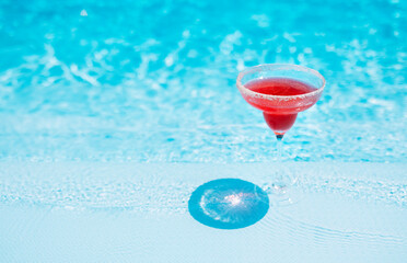 An elegant glass with long stem with a red cocktail. Tasty strawberry drink by the pool. Delicious...