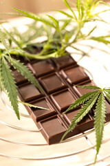 Dark chocolate bar placed beside fresh cannabis leaves on a marble background