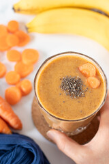 Hand holding carrot banana smoothie with chia seeds on white. Top table view. Healthy orange juice,...