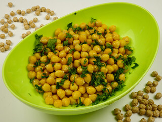 Fresh boiled chick-pea sprinkling with fresh parsley in a green bowl, background