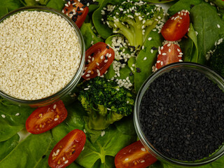 Nutrient seeds.  Flax seeds, black and white sesame seeds in glass bowls and a vegetable salad of spinach leaves, broccoli and cherry tomatoes