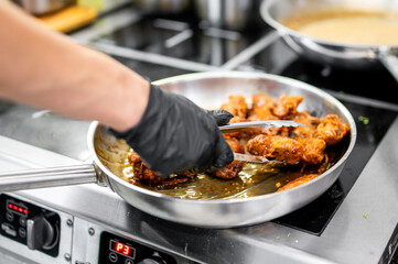 Chef’s gloved hand cooking succulent meat pieces in a sizzling pan, embodying culinary art and gourmet cuisine preparation