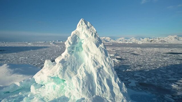 Towering iceberg in Arctic seascape. Giant ice floes, serene beauty of glacier surrounded by pristine icy landscape. Polar frozen ocean, travel to Antarctica. Sunny day blue sky. Aerial drone panorama