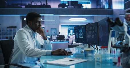 Black Male Neuroscientist Using Desktop Computer To Analyze MRI Scans Of Brain In Medical Research...