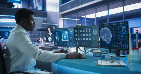 Black Male Neuroscientist Using Desktop Computer To Analyze MRI Scans Of Brain In Medical Research...