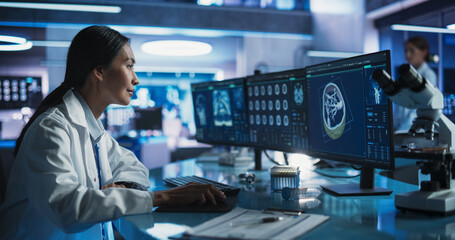 Female Asian Neuroscientist Using Desktop Computer With Human Brain CT Scans In Modern Medical...